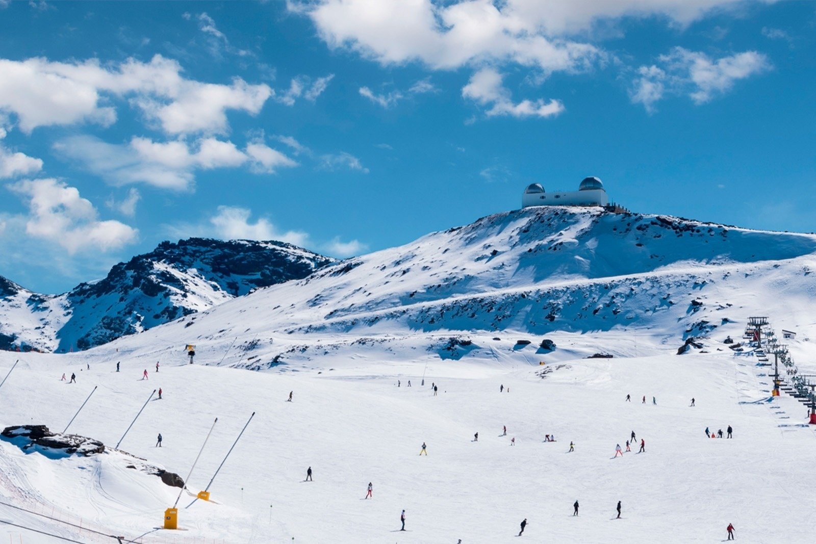 skiers on a snowy slope with a telescope in the background