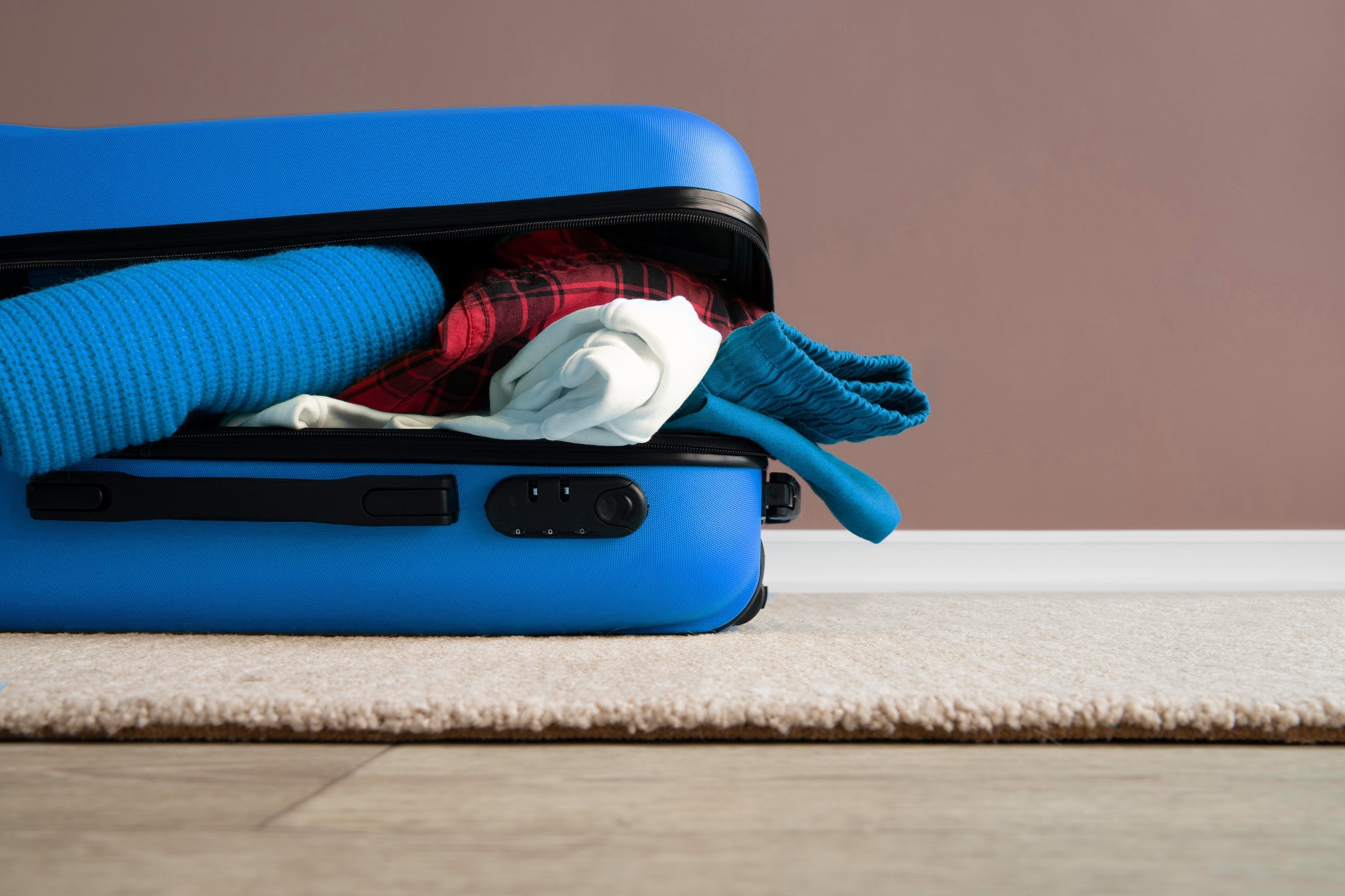 una maleta azul está llena de ropa sobre una alfombra