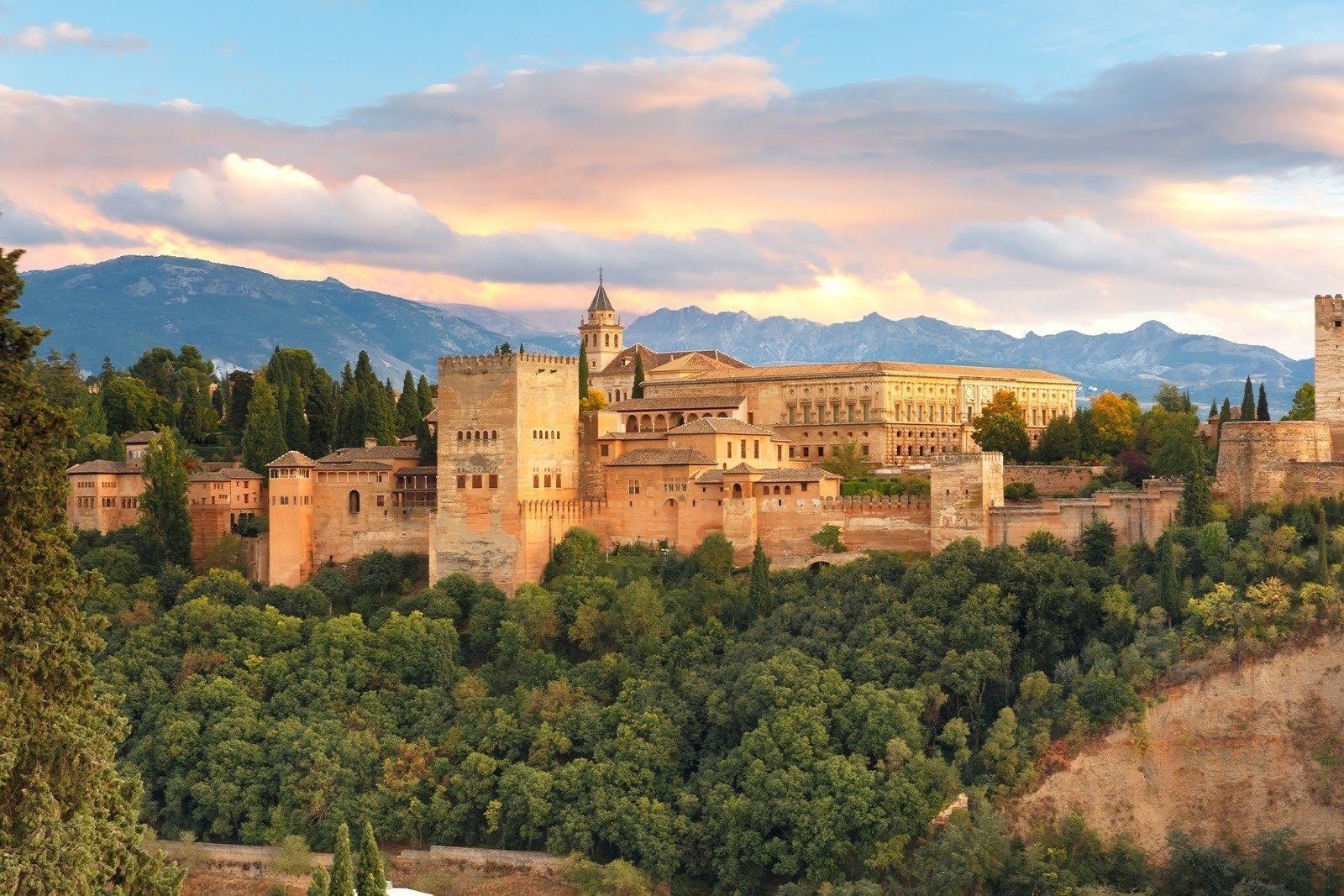 a castle sits on top of a hill with mountains in the background