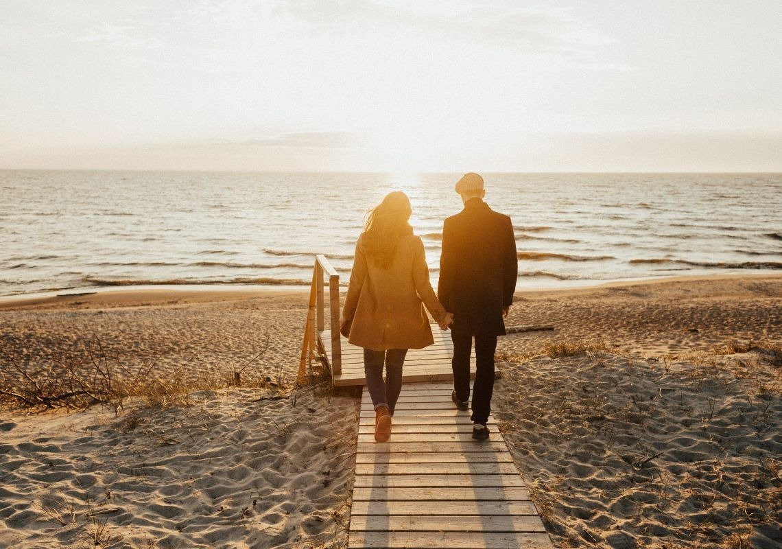 Fuga romantica sulla spiaggia a Port Saplaya: coppia cammina sul pontile al tramonto.