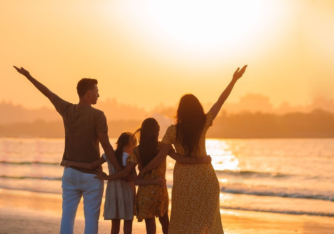 Famiglia felice al tramonto sulla spiaggia, un modo per risparmiare sulle vacanze a Port Saplaya.