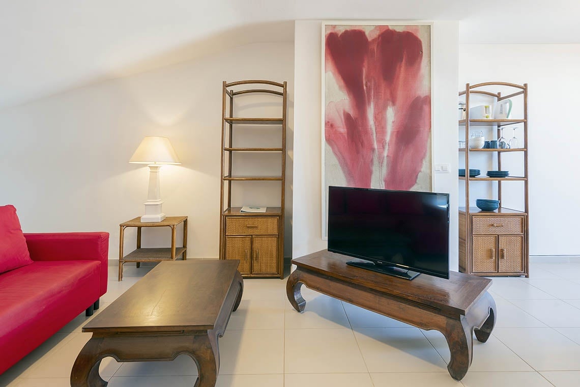 Sea You: Port Saplaya Wohnzimmer mit rotem Sofa und Blumenkunst.