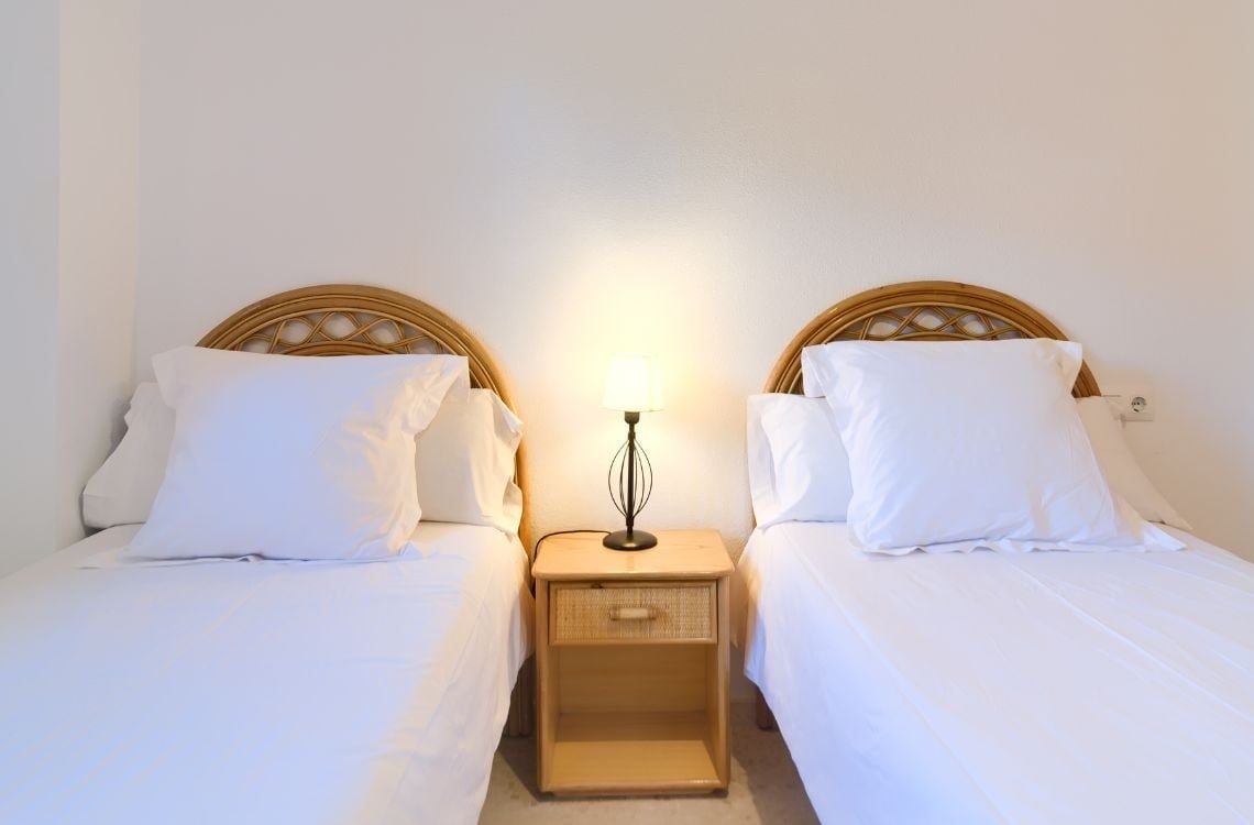 Camere doppie con letti gemelli, comodino e lampada, ideali per vacanze a Sea You: Port Saplaya.