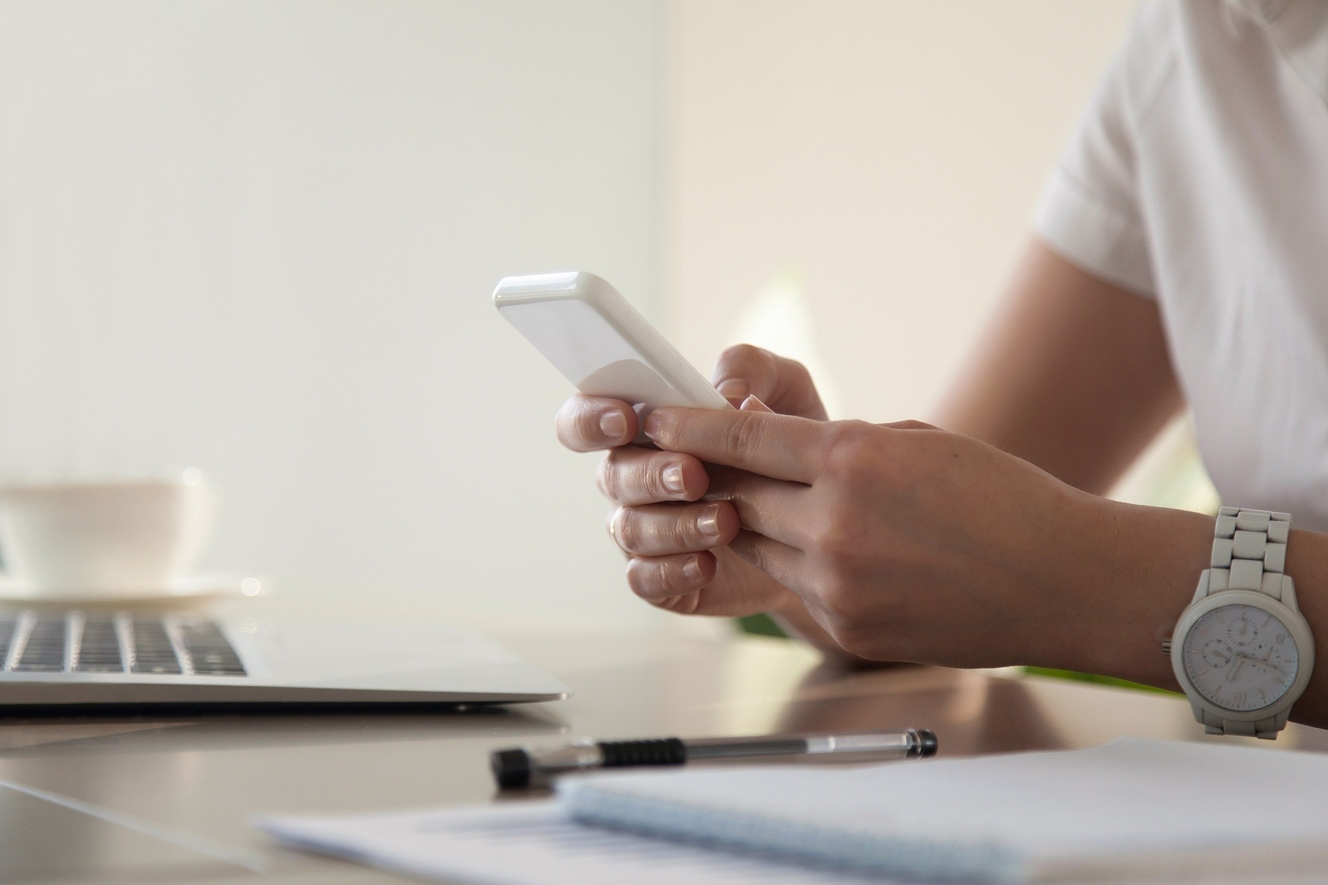 una persona sostiene un teléfono inteligente frente a una computadora portátil