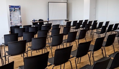 una sala de conferencias llena de sillas negras y una pantalla de proyección - MICE