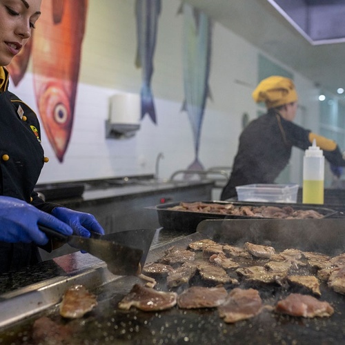 una cocinera sostiene una espátula sobre una parrilla llena de carne