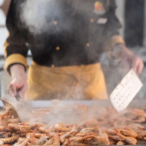 un chef sostiene una espátula sobre una bandeja de camarones