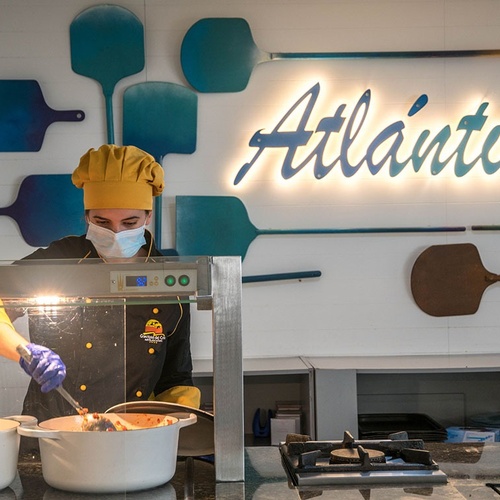 un cocinero prepara comida en una cocina frente a un letrero que dice atlántico