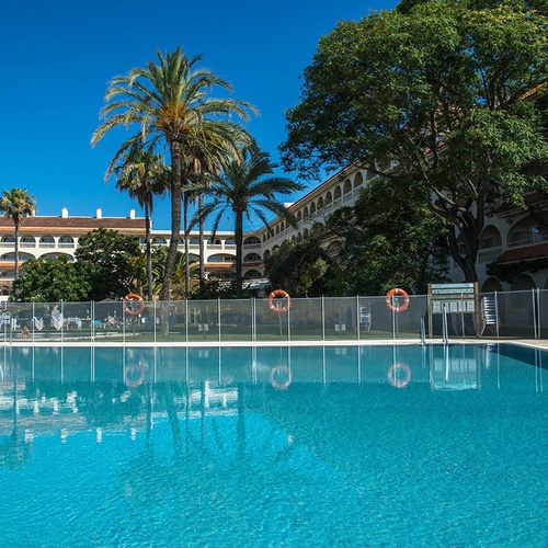 una piscina rodeada de palmeras y un edificio en el fondo