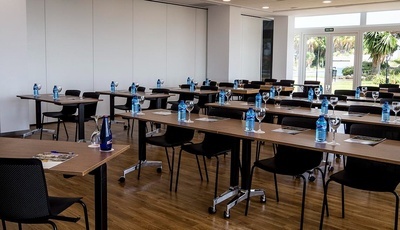una sala de conferencias con mesas y sillas y botellas de agua - MICE