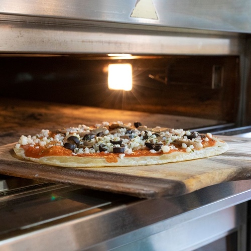una pizza se saca del horno en una tabla de cortar de madera