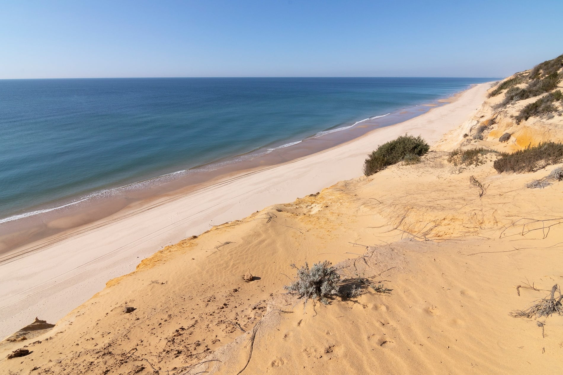 Una playa de arena dorada con palmeras y exuberantes montañas al fondo, donde dos sillas de playa de rayas esperan junto a las tranquilas aguas de un mar azul.