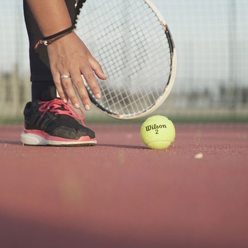 una persona sostiene una raqueta y una pelota de tenis wilson