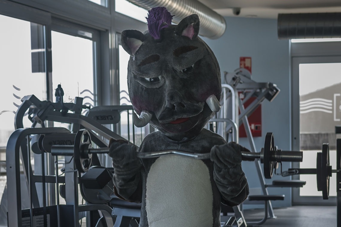 una mascota de un rinoceronte sostiene una barra en un gimnasio