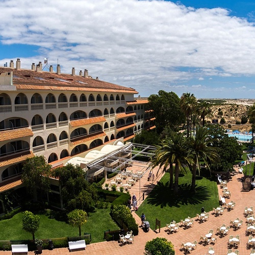 un gran edificio blanco con techos de tejas rojas está rodeado de palmeras y mesas y sillas