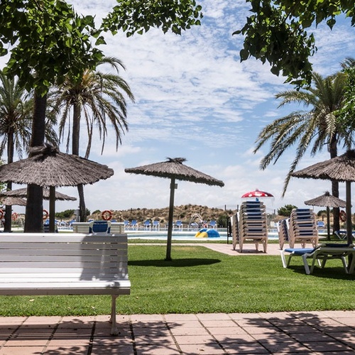un banco blanco está al lado de una piscina rodeada de sillas y sombrillas