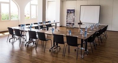 una sala de conferencias con mesas y sillas y una pantalla de proyección - MICE