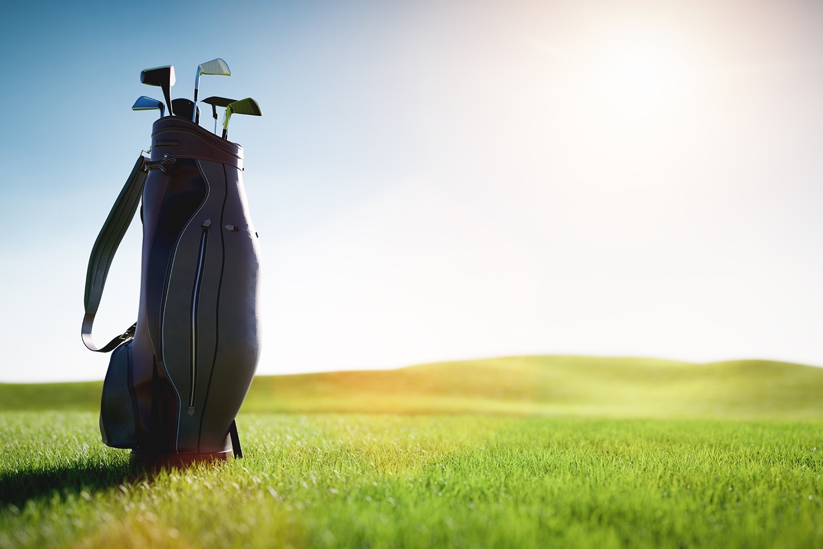 Ein Golfbag mit Schlägern steht auf einem grünen Golfplatz unter einem hellen, sonnigen Himmel.