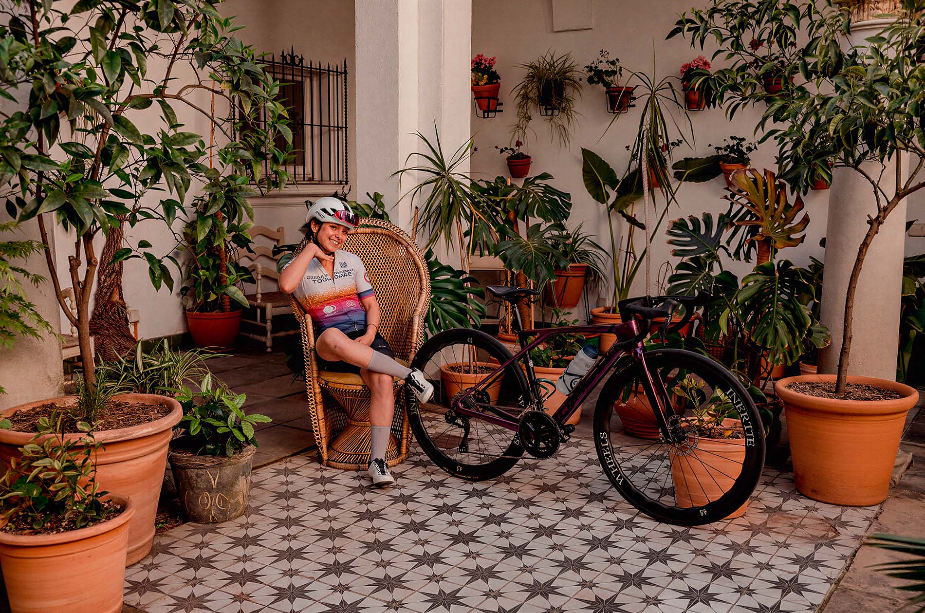 Cycliste souriante dans une cour avec des plantes en pot, idéale pour un séjour Alba Seleqtta.