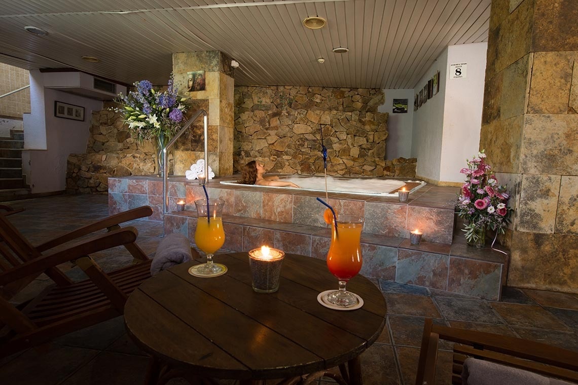 une femme se baigne dans un bain à remous entouré d' une table avec des boissons et des bougies