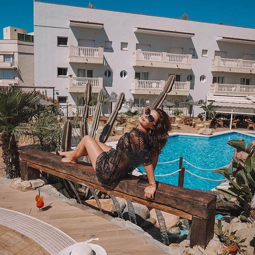 una mujer se sienta en un banco de madera junto a una piscina