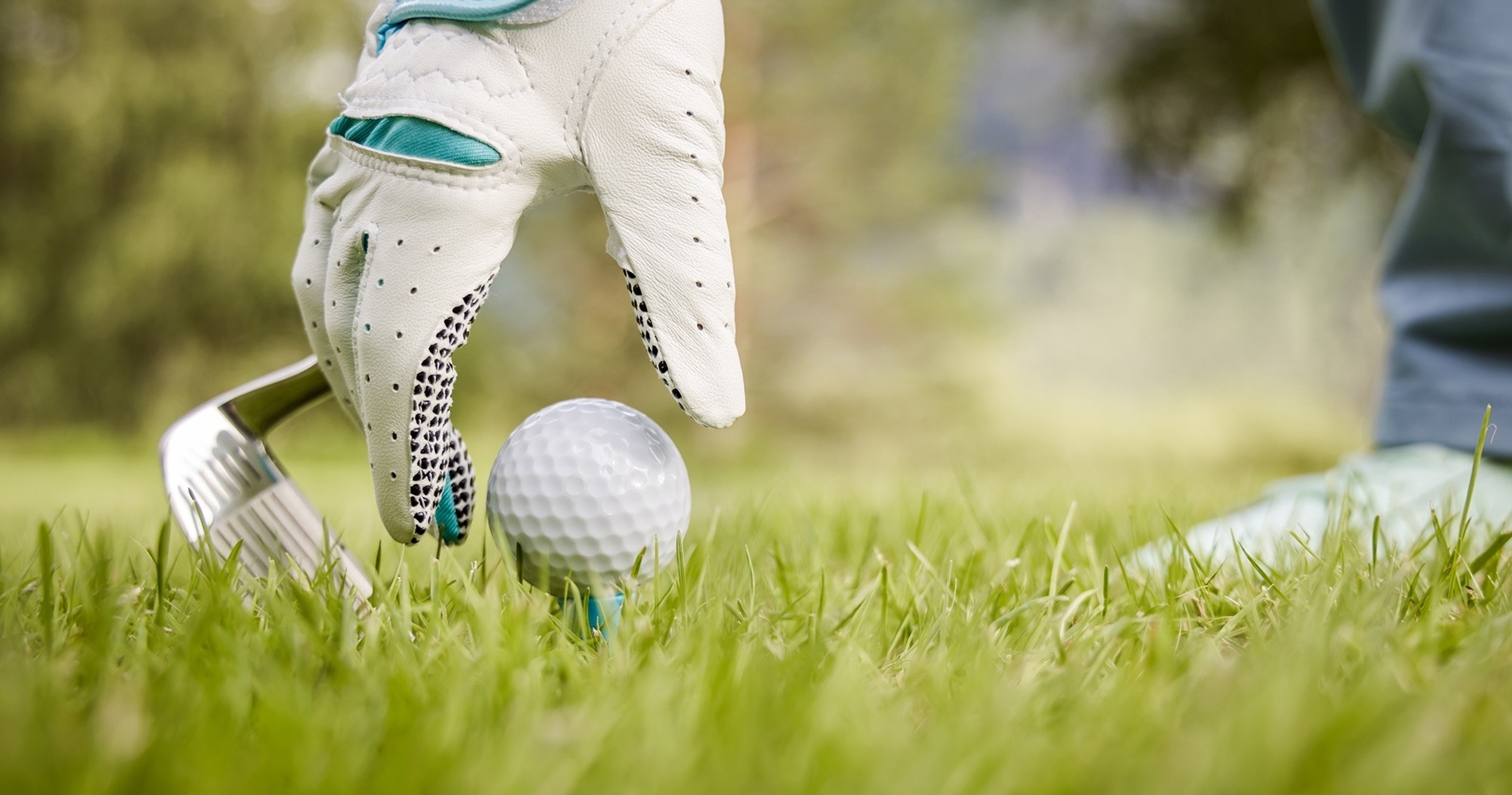 На снимке изображено поле для гольфа с песчаными бункерами и ярко-зеленой травой на фоне деревьев и гор под ясным голубым небом.