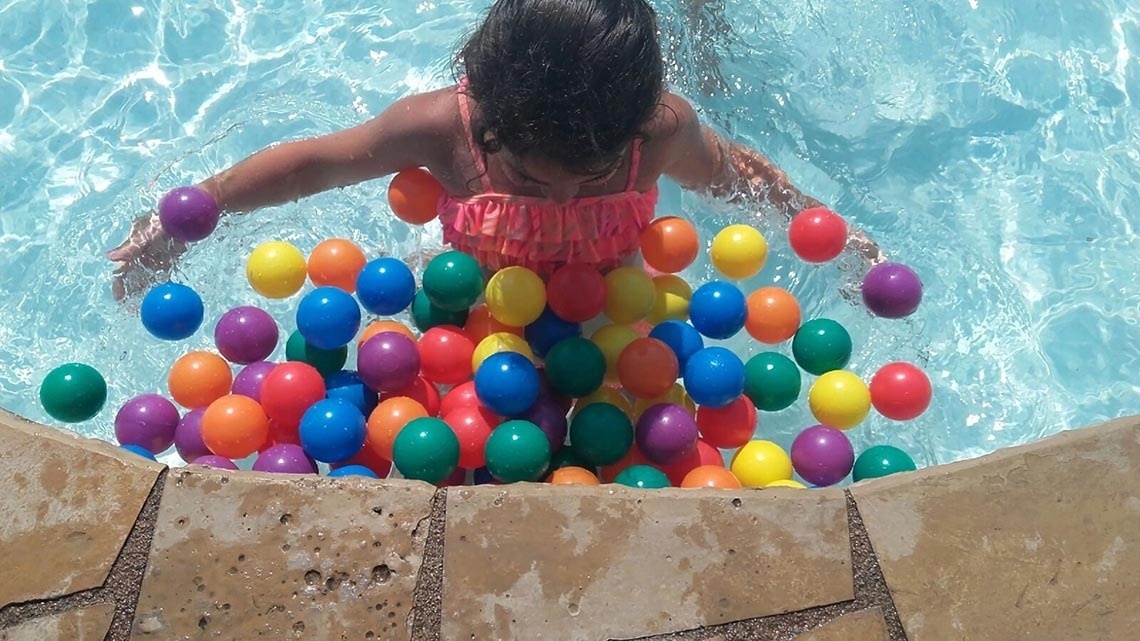 a girl in a pink top is playing in a pool filled with colorful plastic balls