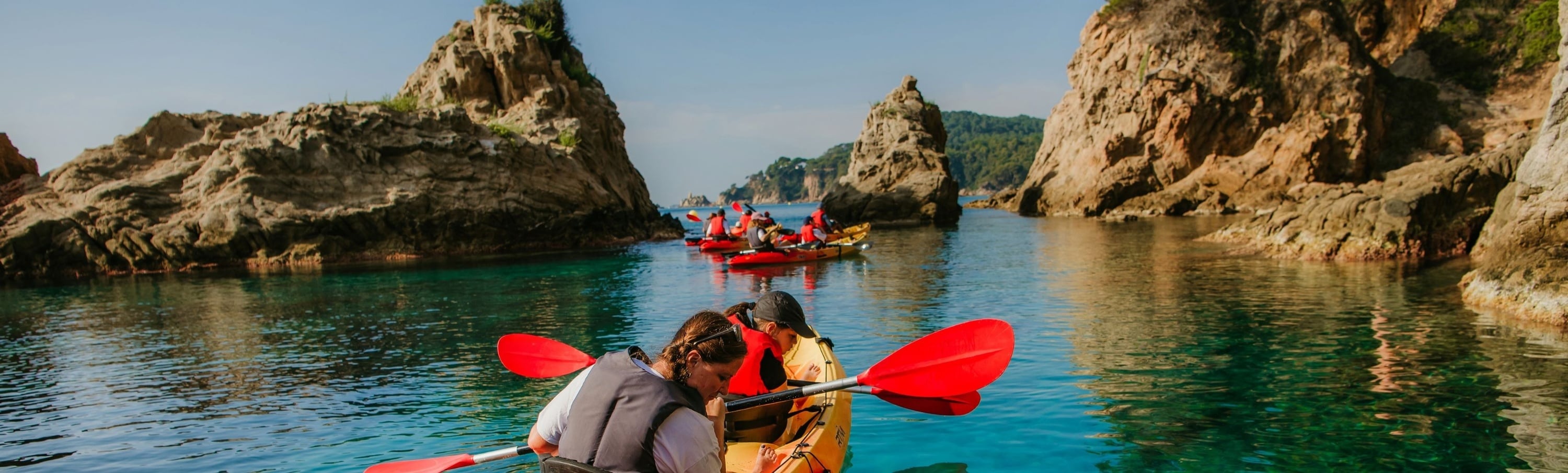 Un grupo de personas está haciendo kayak en aguas tranquilas y claras, rodeadas de imponentes formaciones rocosas.