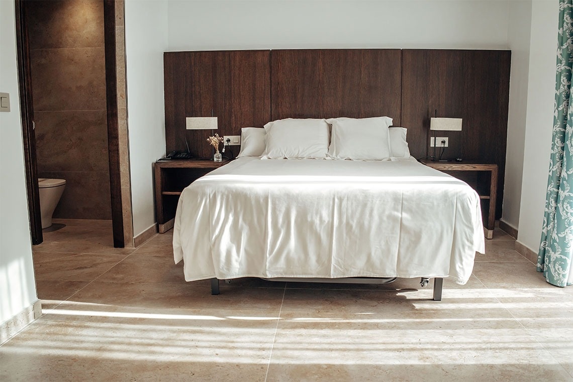 una cama con sábanas blancas y una cabecera de madera