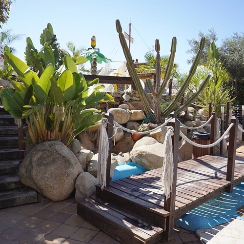 un puente de madera que conduce a una piscina rodeada de rocas y plantas