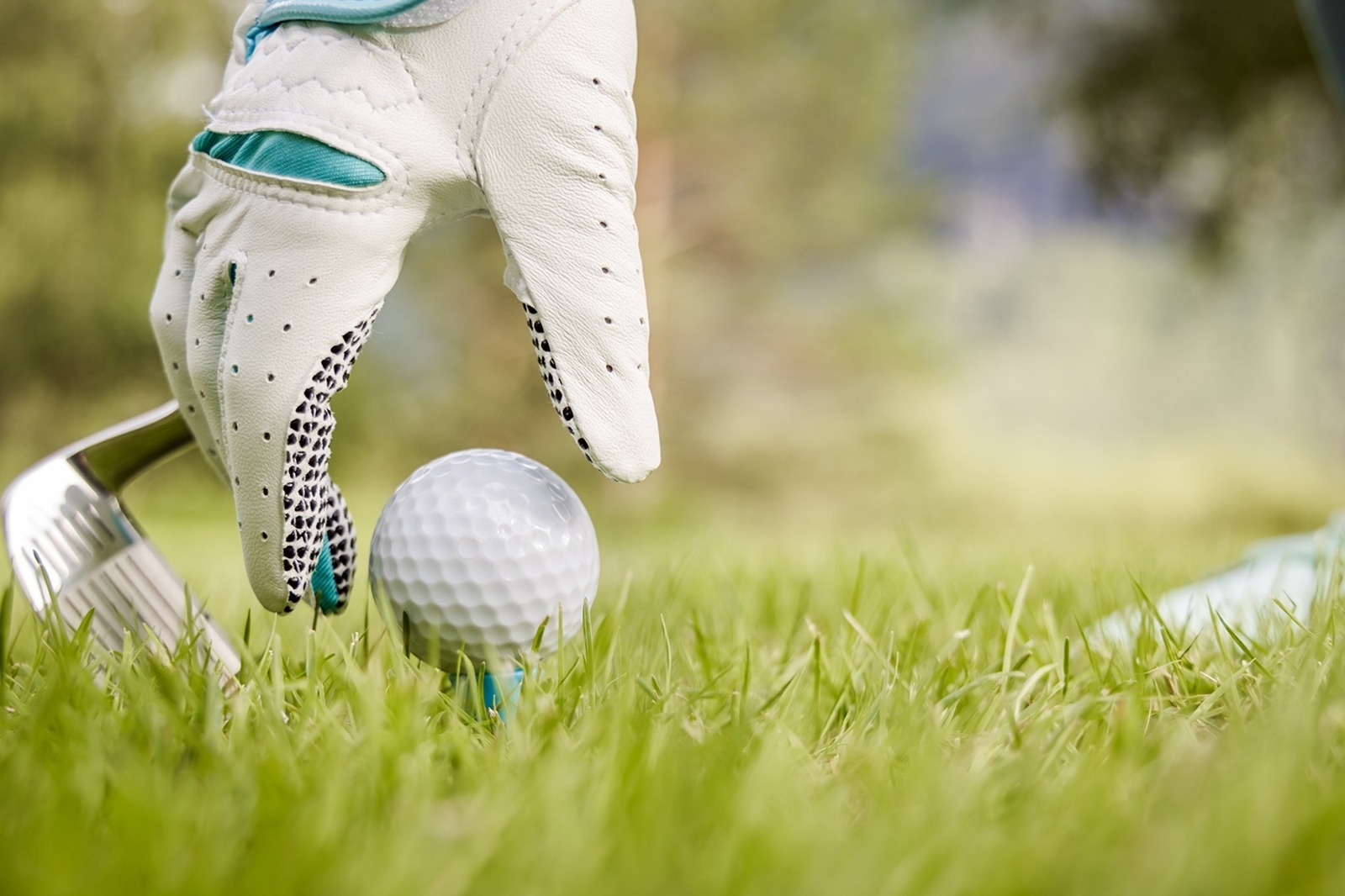 Eine Hand mit einem weißen Golfhandschuh, ein Golfschläger und ein Golfball auf einem Tee sind im grünen Gras abgebildet.