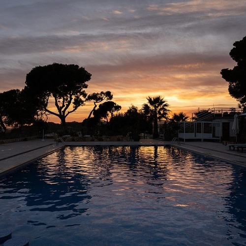 una piscina al atardecer con un cielo naranja en el fondo