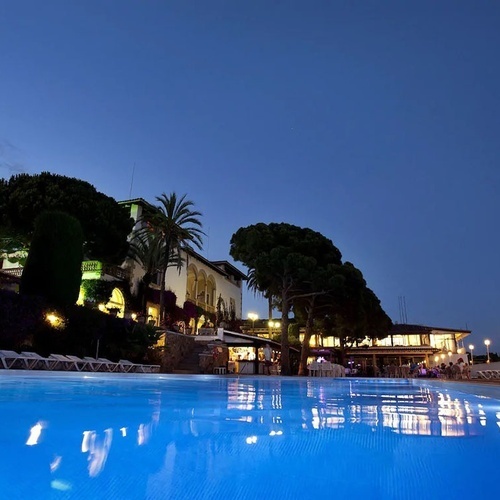 una piscina iluminada por la noche con un gran edificio en el fondo