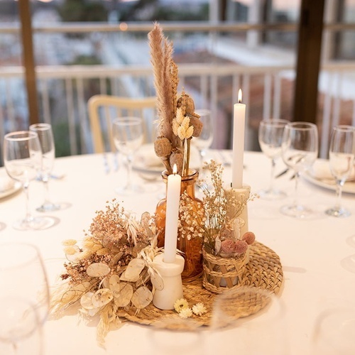 una mesa con copas de vino y un jarrón lleno de flores secas y velas