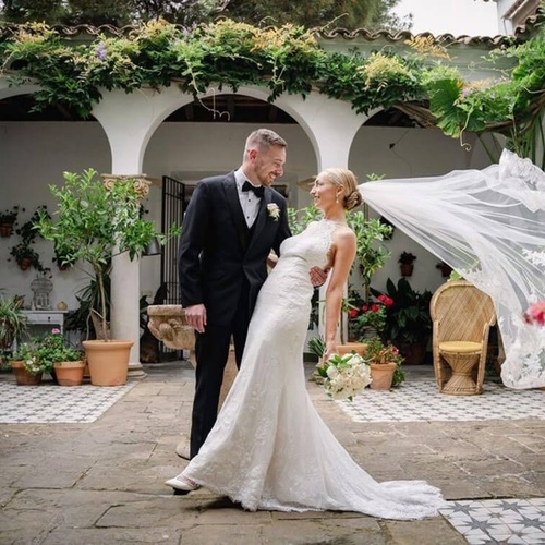 una novia y un novio posan para una foto mientras el velo de la novia sopla en el viento