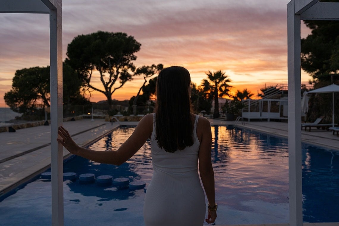 a woman in a white dress stands in front of a pool at sunset