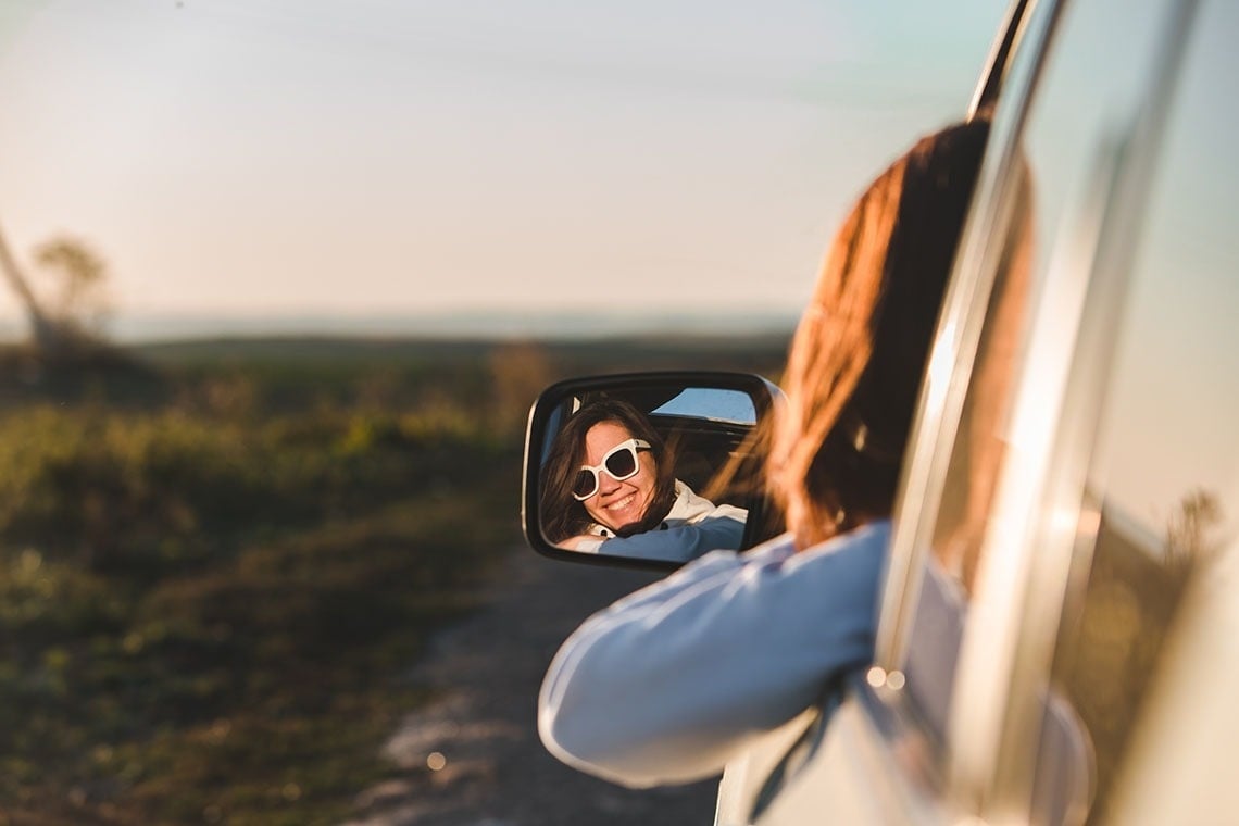 a woman wearing sunglasses is smiling in the rear view mirror of her car
