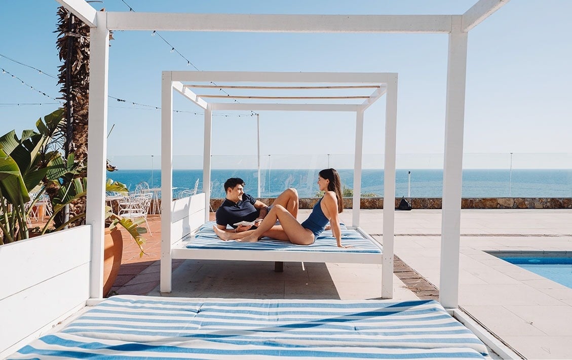 a man and a woman are laying on a canopy bed overlooking the ocean