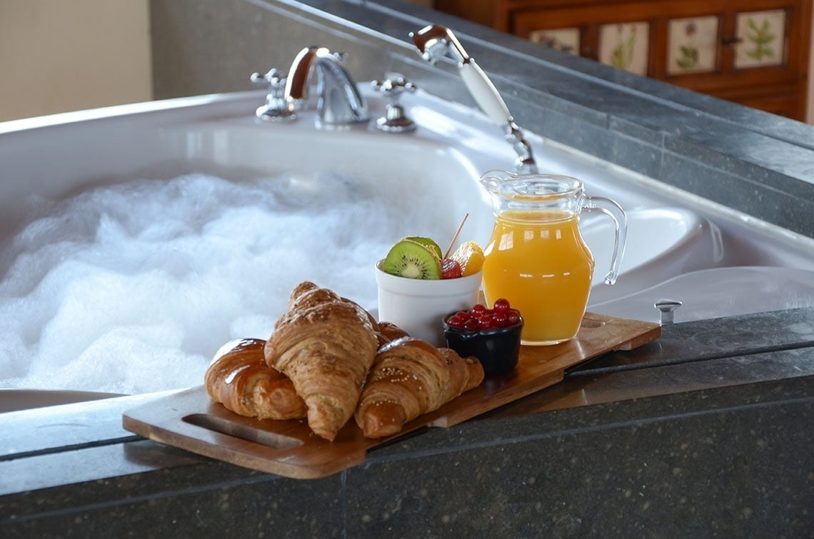 una bañera llena de espuma con una bandeja de madera con croissants y zumo de naranja
