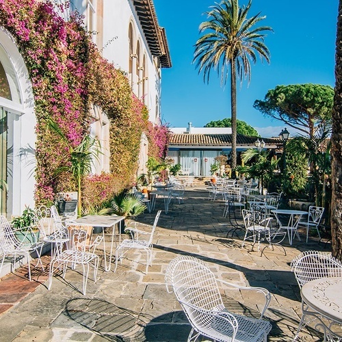 un patio con mesas y sillas frente a un edificio blanco