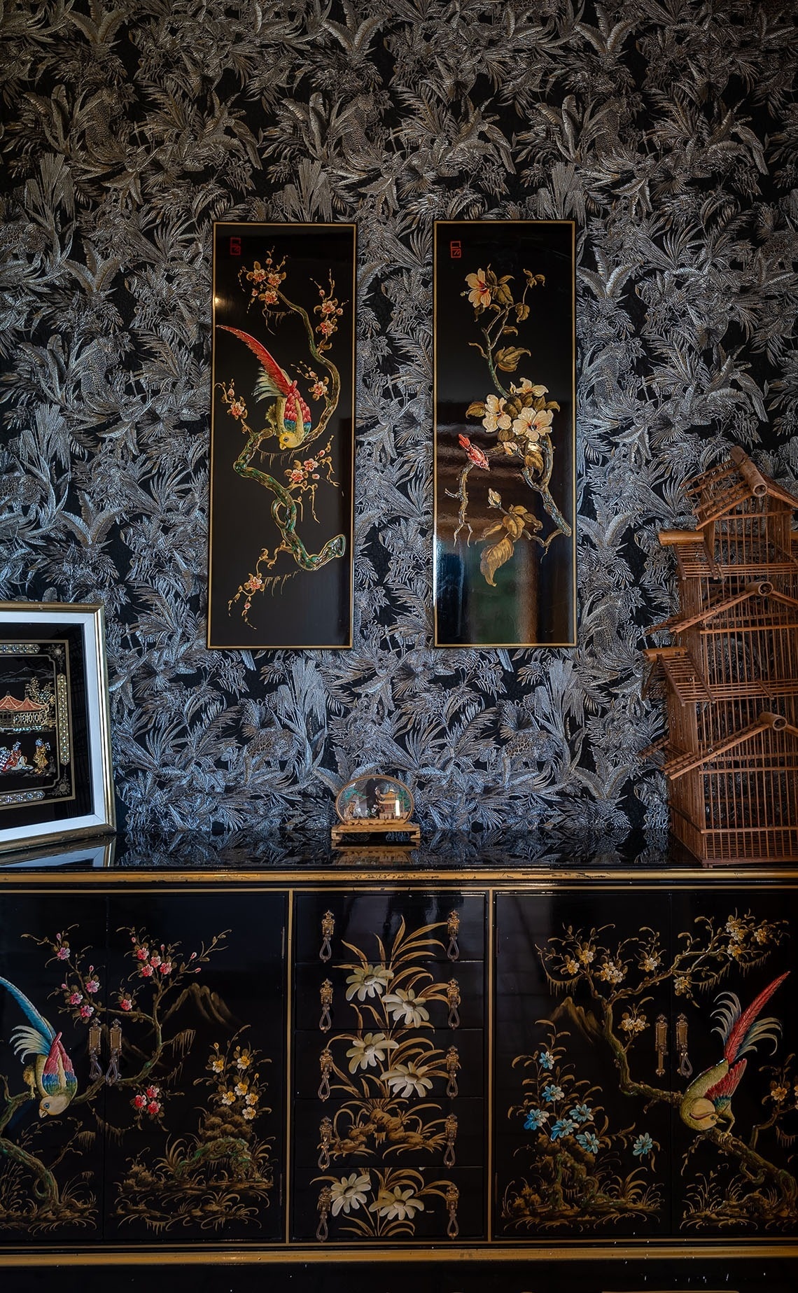 dos cuadros de pájaros y flores están colgados en una pared junto a una jaula de pájaros