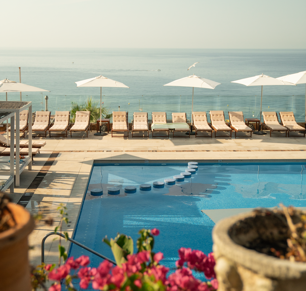 Los novios posan en un hermoso patio con arcos y vegetación, con el velo de la novia ondeando al viento.