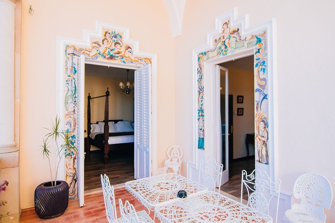 una mesa y sillas en un balcón con una cama en el fondo