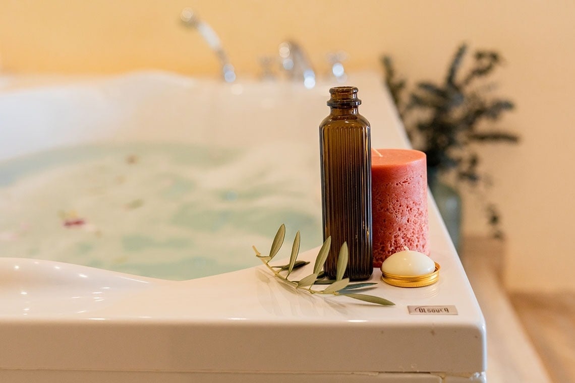 una botella de aceite y una vela junto a una bañera