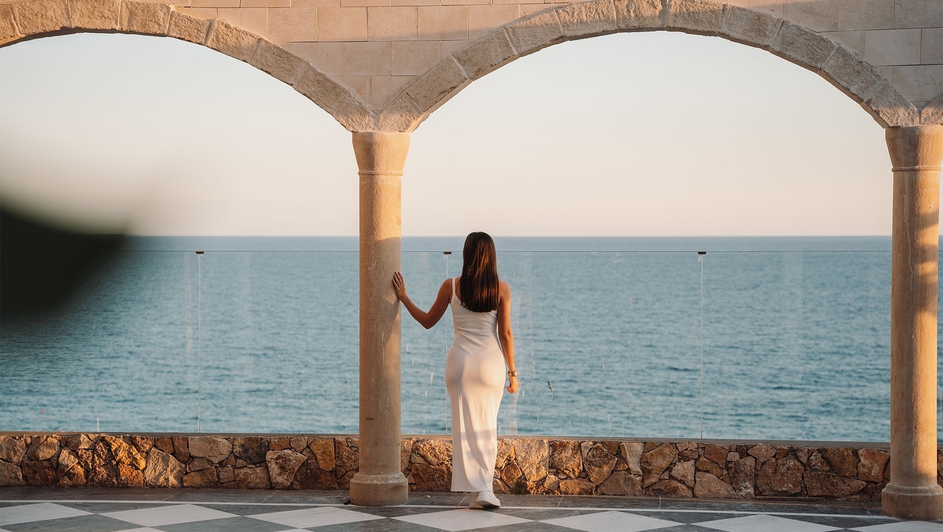 a woman in a white dress stands on a balcony overlooking the ocean