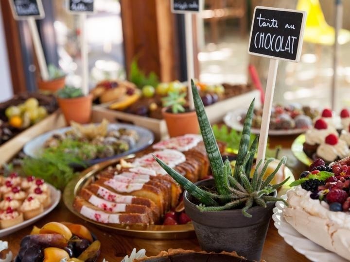 une table remplie de plats et de gâteaux avec une plante en pot à côté d' un panneau qui dit tarte au chocolat