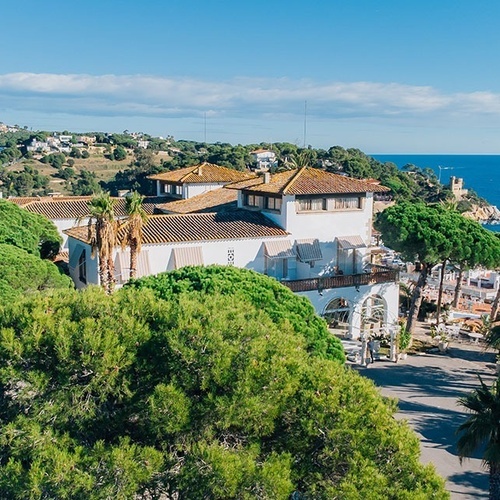 una gran casa blanca está rodeada de árboles y palmeras junto al océano
