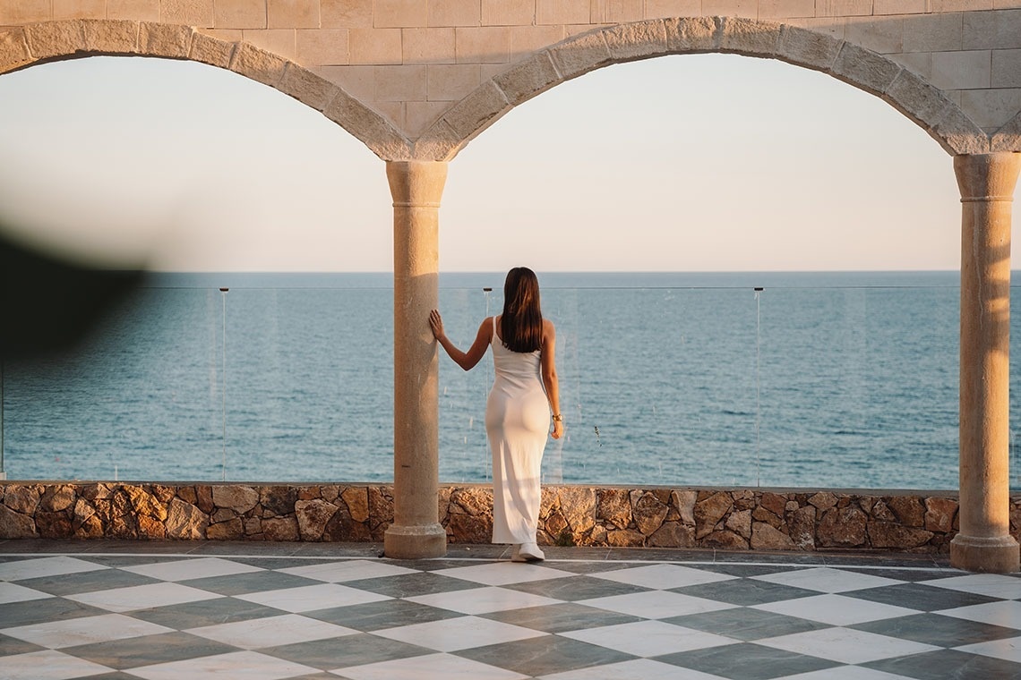 a woman in a white dress stands on a balcony overlooking the ocean