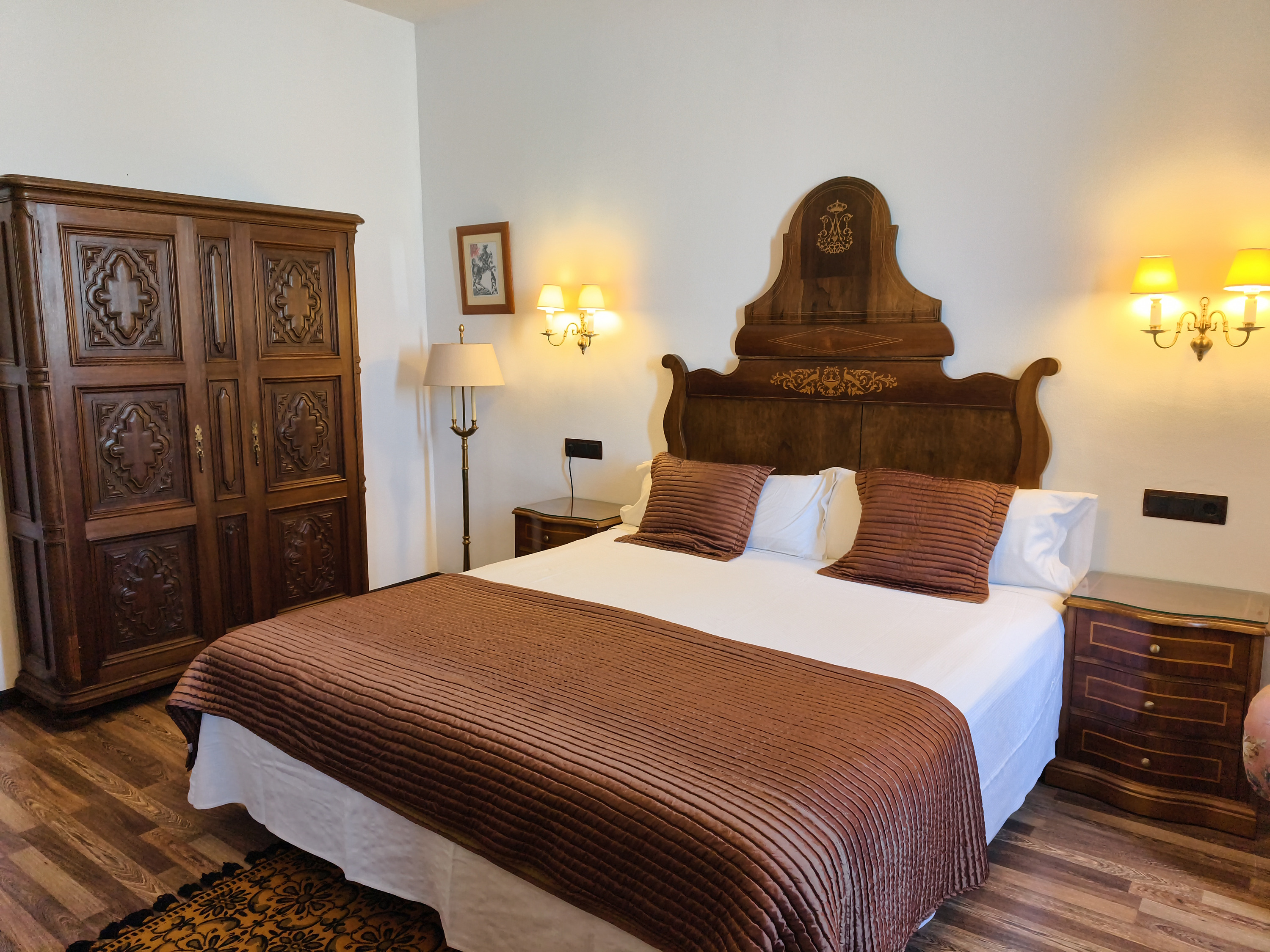 Elegant hotel room with antique wardrobe, ornate wooden bed, and cozy brown bedding. Roger De Flor By Seleqtta