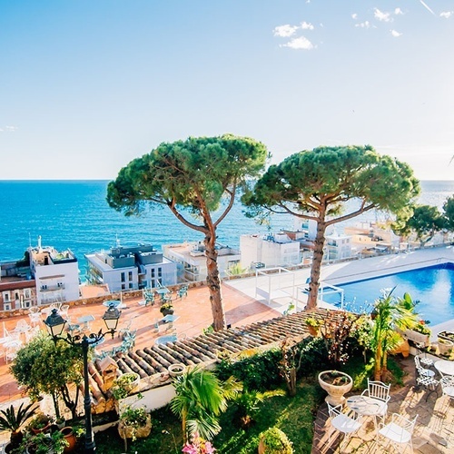 una piscina rodeada de árboles y mesas con vistas al océano